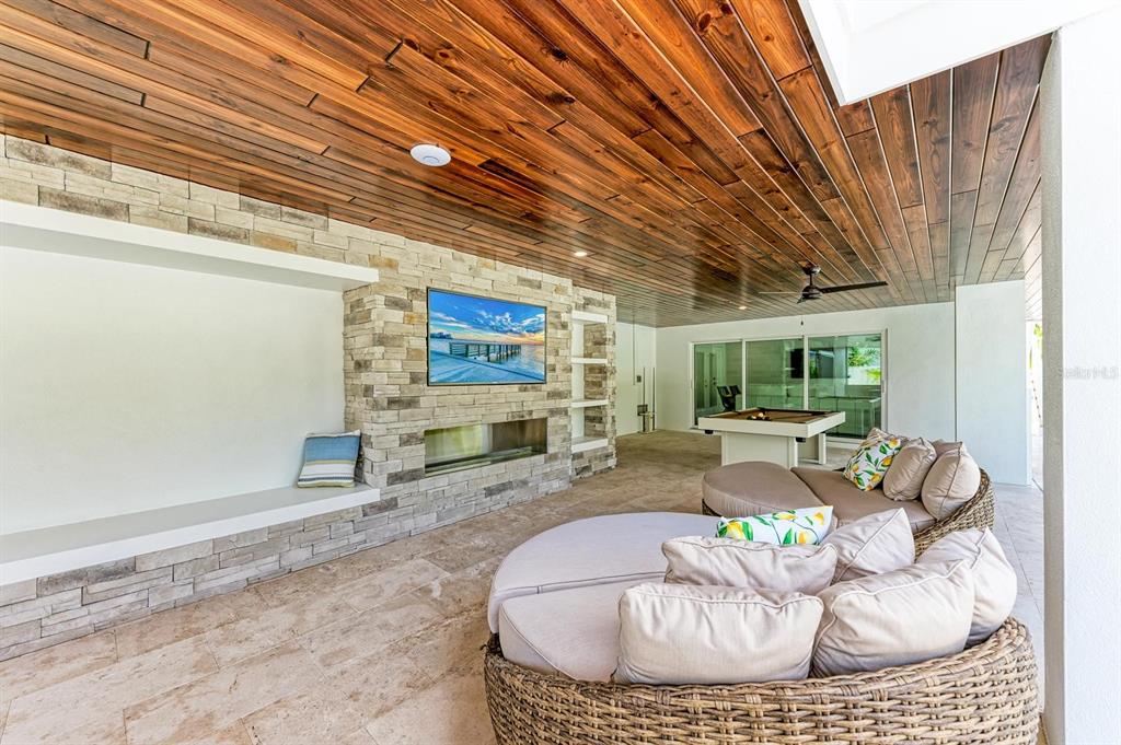 A covered outdoor patio features a stone fireplace, a wall-mounted television, and circular lounge seating — 215 83RD STREET, HOLMES BEACH, FL