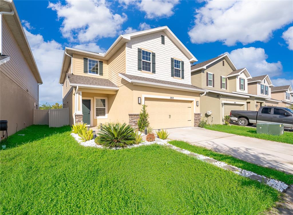 A two-story suburban house with tan siding, a white shingled gable, and a two-car garage — 3852 SAGEFIELD DRIVE, HARMONY, FL