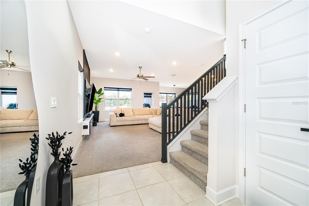An entryway with tiled flooring leads to a carpeted living room with a staircase — 3852 SAGEFIELD DRIVE, HARMONY, FL