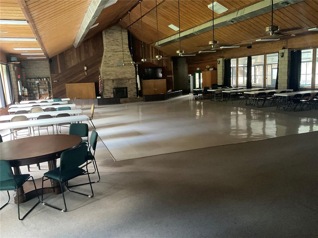 A large community hall features a brick fireplace, wood-paneled walls, and rows of tables — 25289 NE 140TH LANE NE UNIT 363, SALT SPRINGS, FL