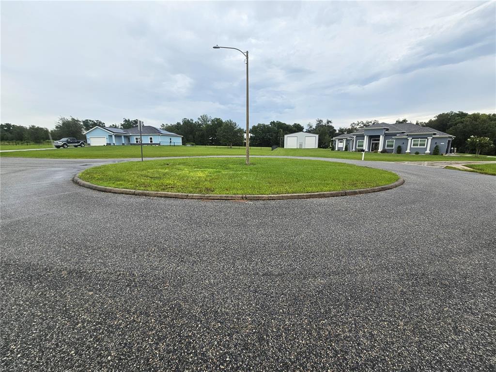 A paved cul-de-sac features a central grassy island with a street lamp — 8801 VALERIE COURT, ZEPHYRHILLS, FL