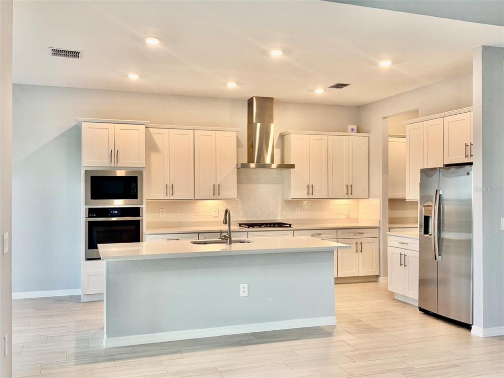 A modern kitchen features white cabinets, stainless steel appliances, a center island, and light flooring — 19227 SCALLOP LOOP, LAKEWOOD RANCH, FL