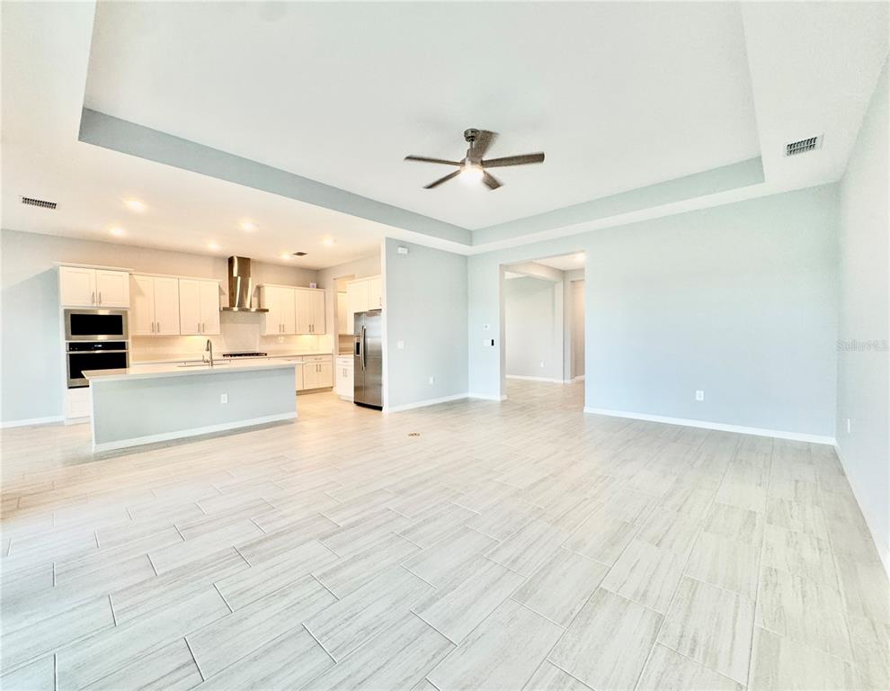 An open-concept kitchen and living area featuring white cabinetry, stainless steel appliances, and tile flooring — 19227 SCALLOP LOOP, LAKEWOOD RANCH, FL