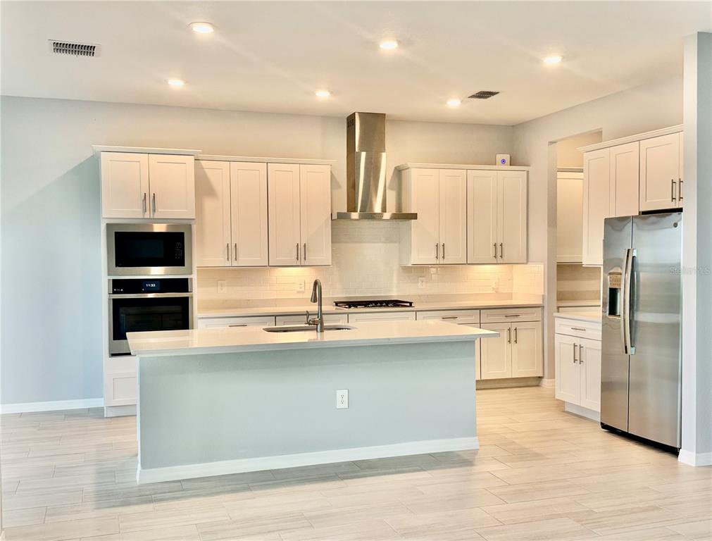 A modern kitchen features white cabinetry, stainless steel appliances, a center island, and tile flooring — 19227 SCALLOP LOOP, LAKEWOOD RANCH, FL
