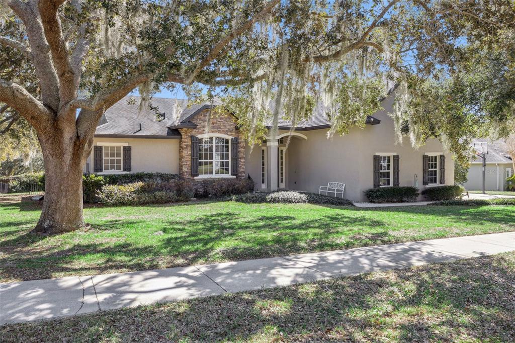 A single-story house with a stone facade, dark shutters, and a large oak tree out front — 11526 OSPREY POINTE BOULEVARD, CLERMONT, FL