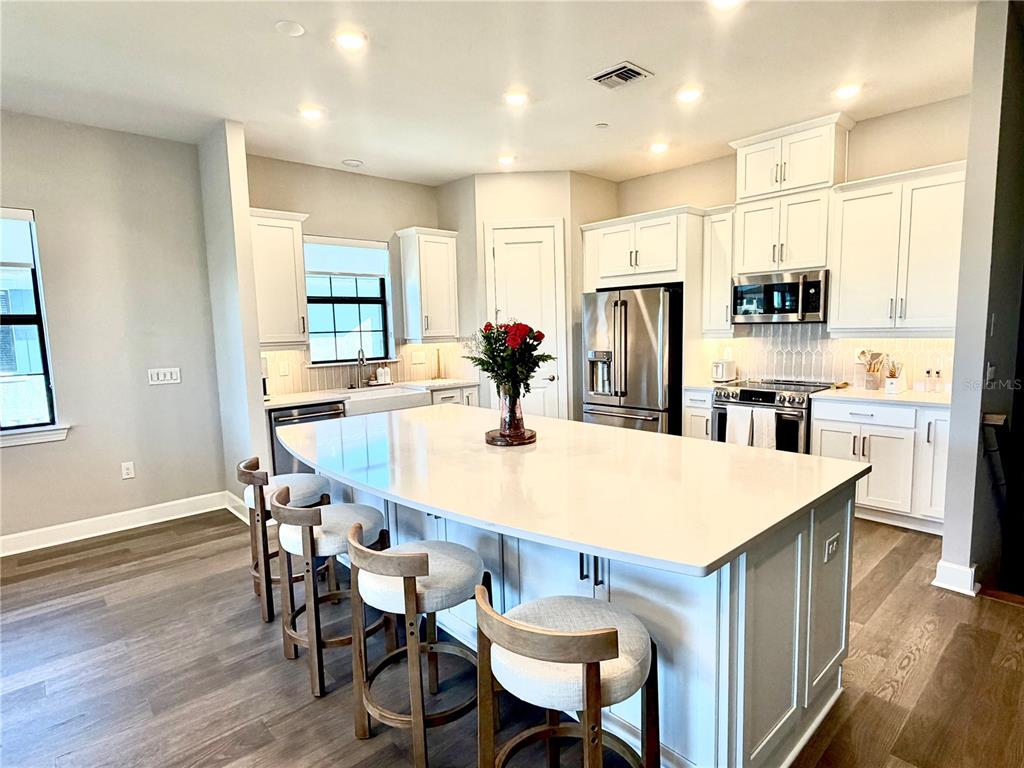 A modern kitchen features white cabinetry, a large quartz island with bar stools, and wood flooring — 15323 LUCERNA STREET UNIT 204, NAPLES, FL