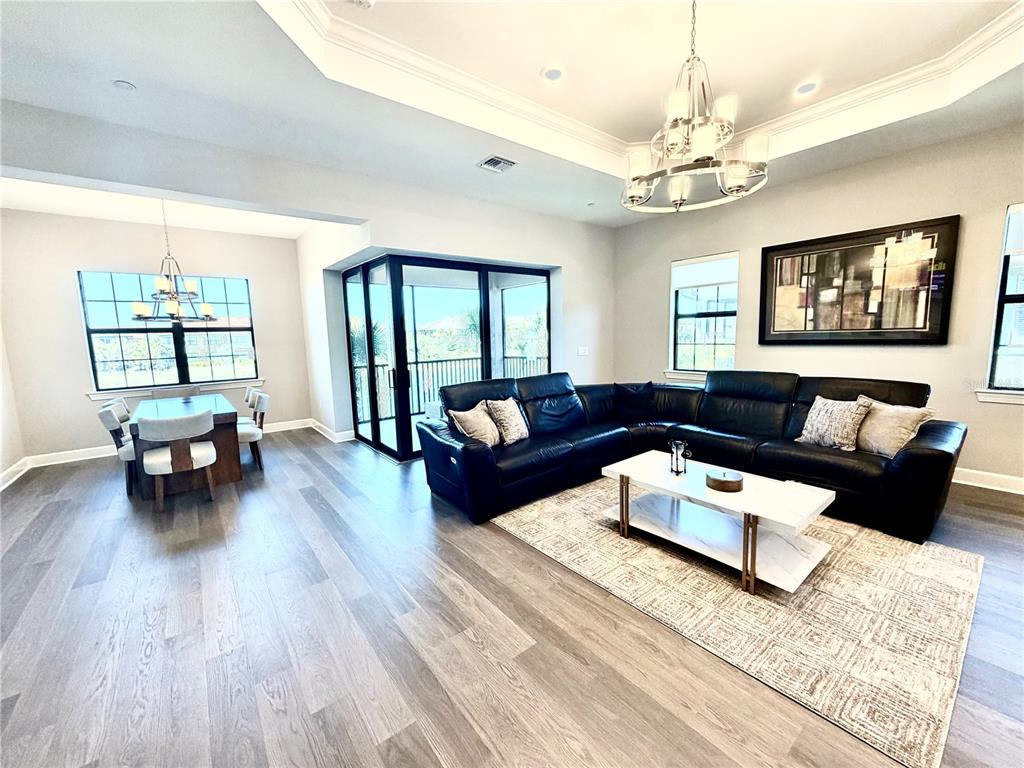 A living and dining area features gray wood-look flooring, a black sectional sofa, and a chandelier — 15323 LUCERNA STREET UNIT 204, NAPLES, FL