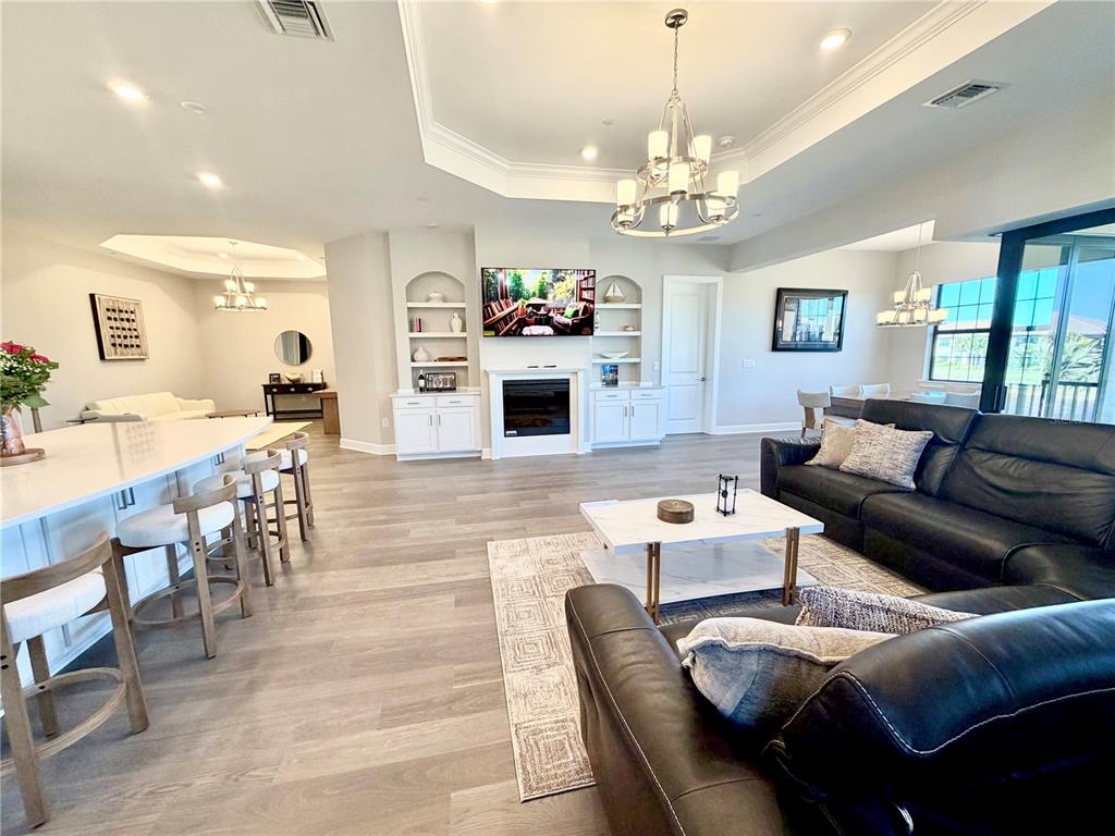An open-concept living room features a fireplace, built-in shelving, a kitchen island, and leather furniture — 15323 LUCERNA STREET UNIT 204, NAPLES, FL
