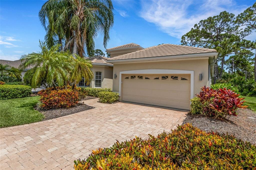 A beige house with a two-car garage, a paver driveway, and lush tropical landscaping — 299 TURQUOISE LANE, OSPREY, FL