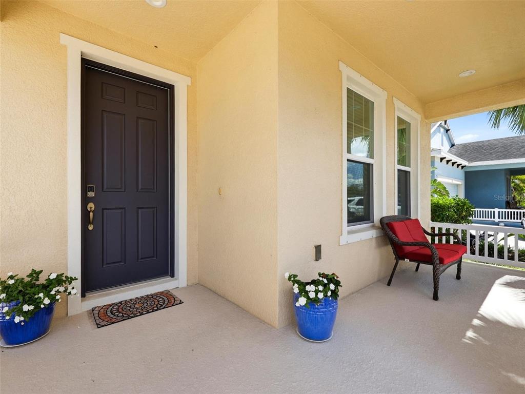 A covered front porch features a dark door, a red wicker chair, and blue planters — 5133 ADMIRAL POINTE DRIVE, APOLLO BEACH, FL