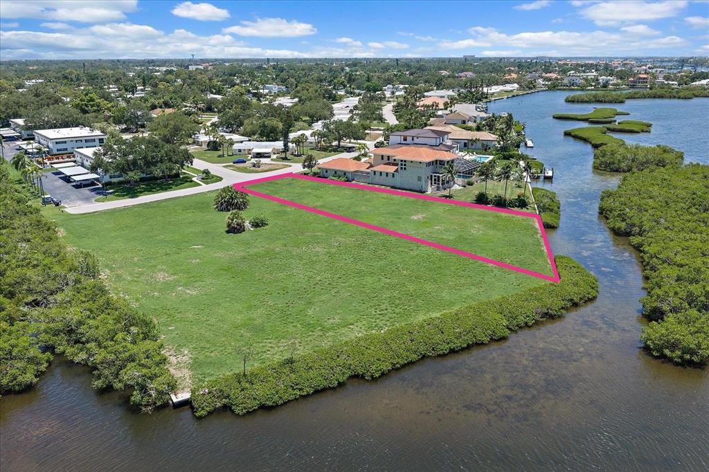 An aerial view shows a vacant, grassy waterfront lot outlined in pink near residential homes — TIDEWOOD AVENUE, SARASOTA, FL