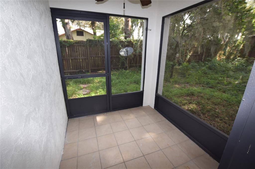 A tiled screened-in porch overlooks a wooded backyard with a wooden fence — 908 SUMTER STREET, LEESBURG, FL