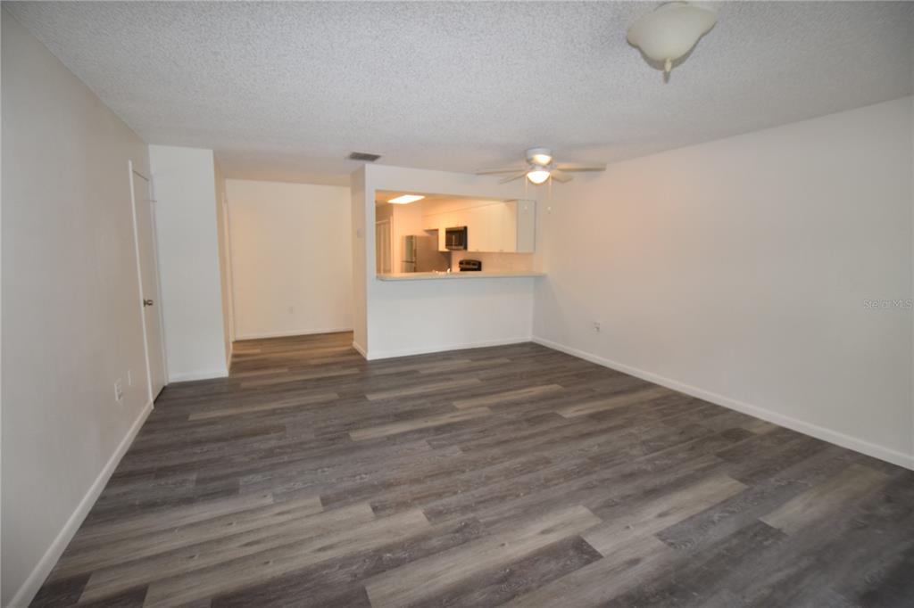 A living room with gray wood-look flooring, a ceiling fan, and a kitchen pass-through window — 908 SUMTER STREET, LEESBURG, FL
