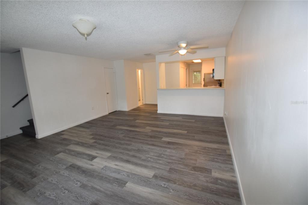An unfurnished living room features gray wood-look flooring, white walls, and a kitchen pass-through window — 908 SUMTER STREET, LEESBURG, FL