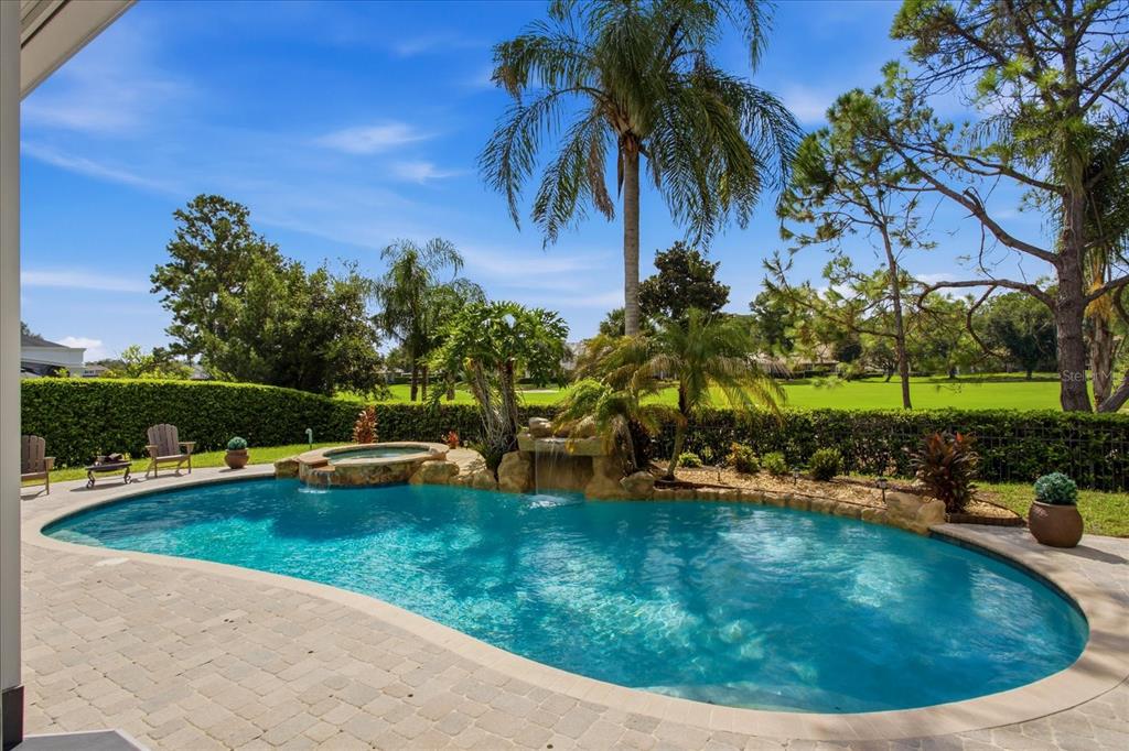 A backyard swimming pool with a rock waterfall and spa overlooks a green golf course — 8241 TIBET BUTLER DRIVE, WINDERMERE, FL