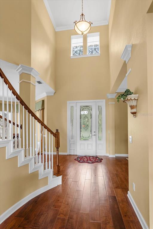 A high-ceilinged foyer features hardwood floors, a staircase with white railings, and a decorative front door — 8241 TIBET BUTLER DRIVE, WINDERMERE, FL