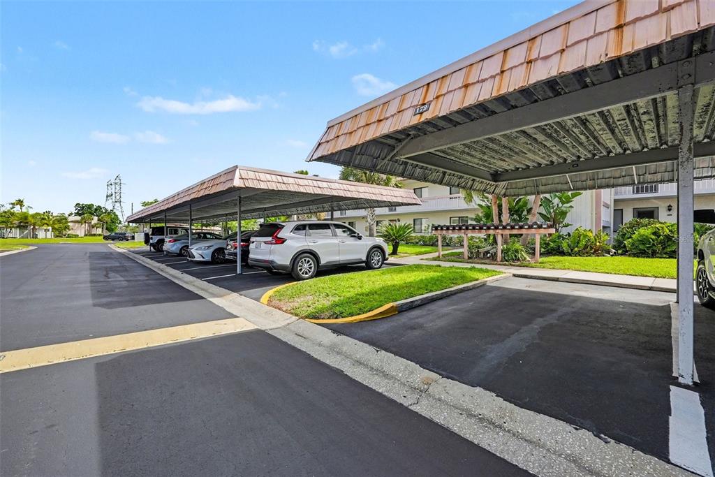 A parking lot features two covered carports with parked vehicles and a nearby apartment building — 172 LAKEVIEW WAY UNIT 172, OLDSMAR, FL