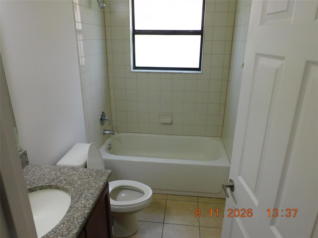 A bathroom features a granite-topped vanity, a white toilet, and a tiled shower-tub combination — 2916 CASABELLA DRIVE, KISSIMMEE, FL