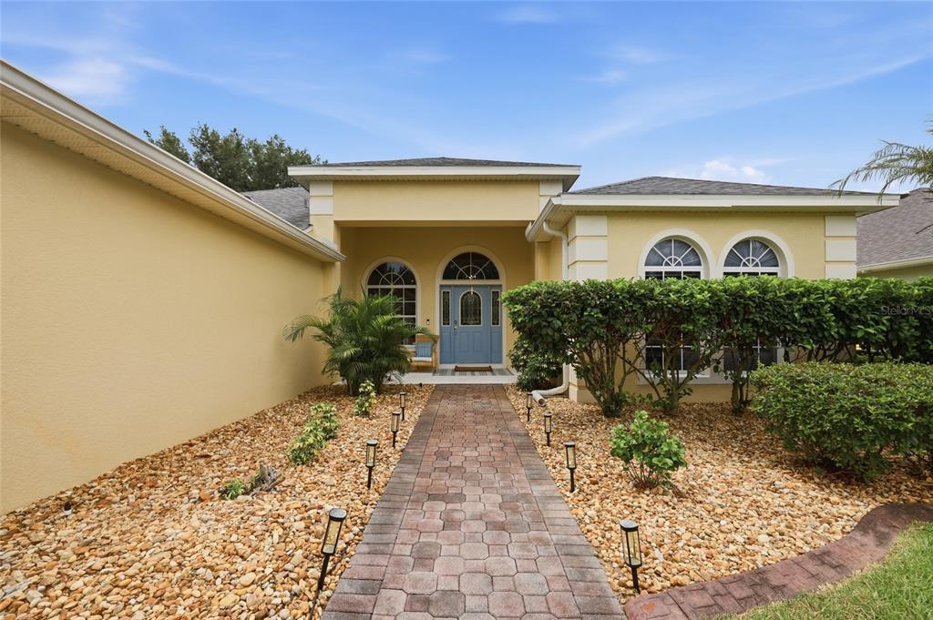A paved walkway leads to the blue front door of a yellow stucco house — 3790 LIBERTY HILL DRIVE, CLERMONT, FL