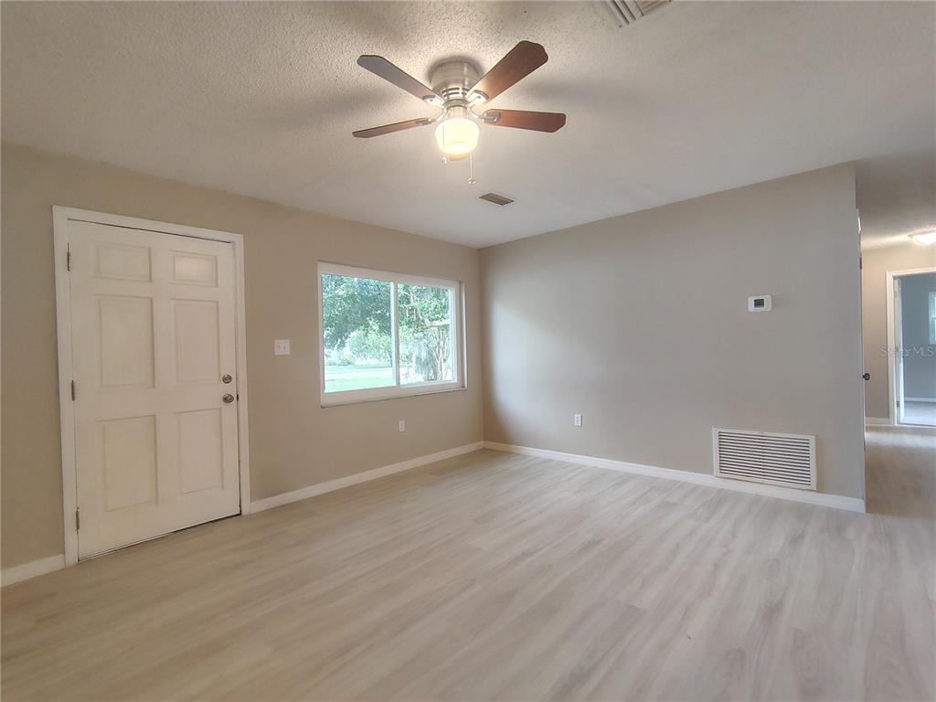 An empty room features light wood-look flooring, a ceiling fan, and a white front door — 904 HICKORY AVENUE, FRUITLAND PARK, FL