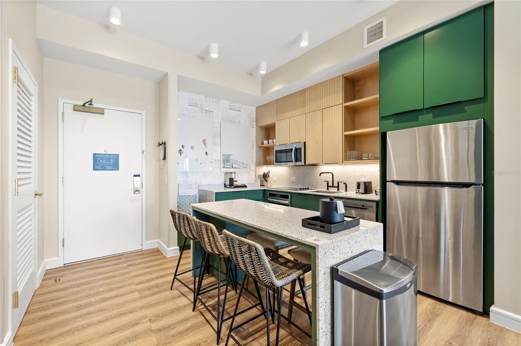 A kitchen features a granite island, stainless steel appliances, and green cabinetry with wood accents — 3151 SUNSET WALK DRIVE UNIT 508, KISSIMMEE, FL