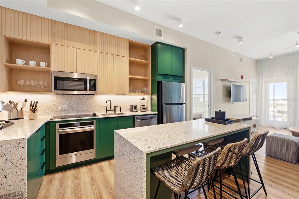 A modern kitchen features green cabinets, light wood accents, speckled countertops, and a breakfast island — 3151 SUNSET WALK DRIVE UNIT 508, KISSIMMEE, FL