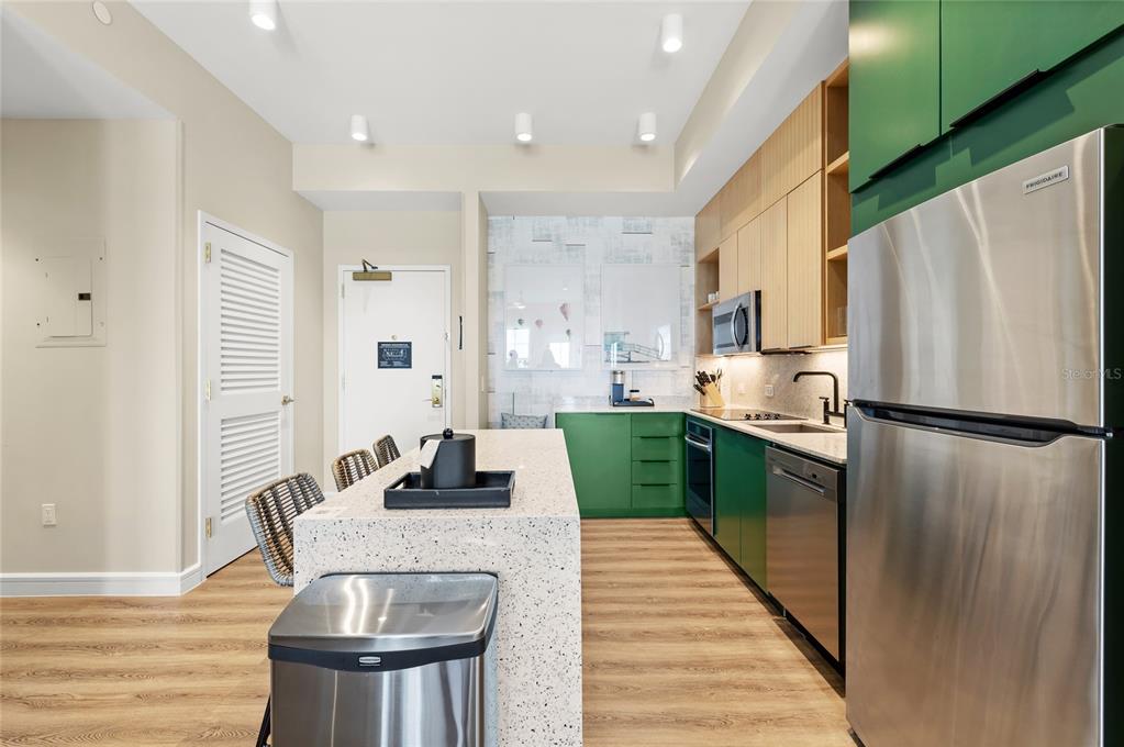 A modern kitchen features green cabinets, stainless steel appliances, and a speckled stone island — 3151 SUNSET WALK DRIVE UNIT 508, KISSIMMEE, FL