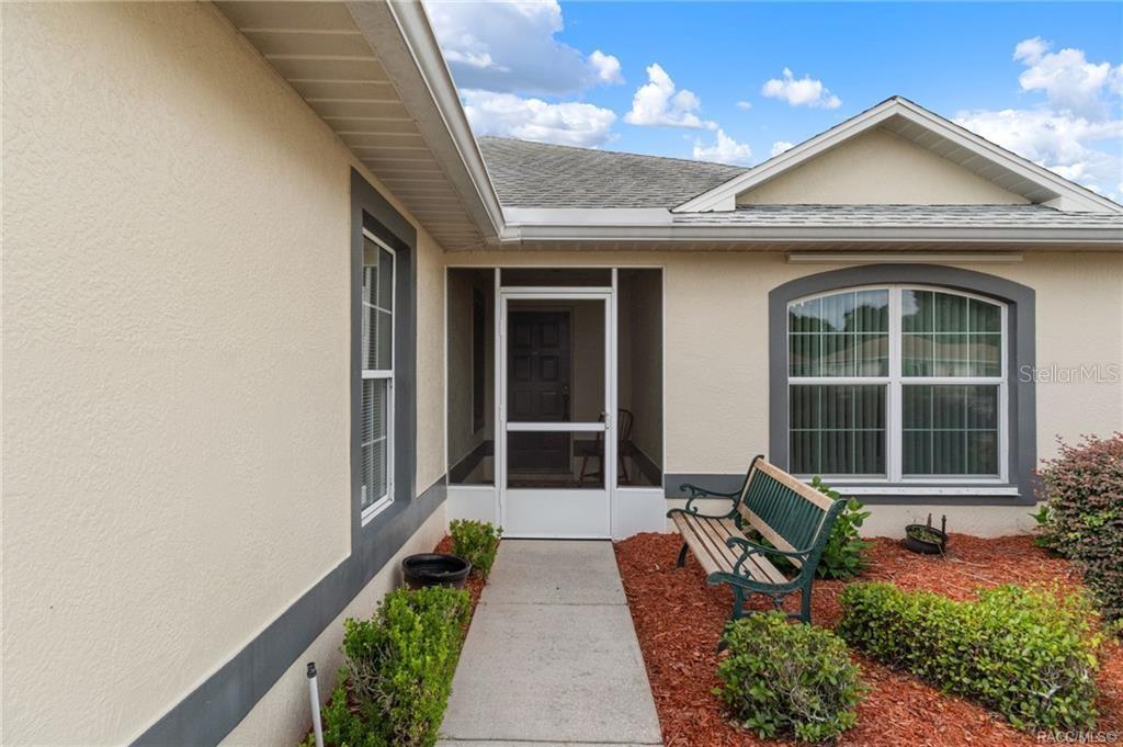 A concrete walkway leads to a screened front entryway with a bench and landscaping — 3676 E IBIS COVE COURT, HERNANDO, FL