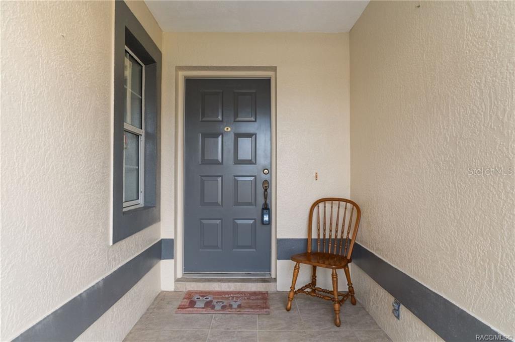 A covered entryway features a gray door, a wooden chair, and a small owl-themed mat — 3676 E IBIS COVE COURT, HERNANDO, FL