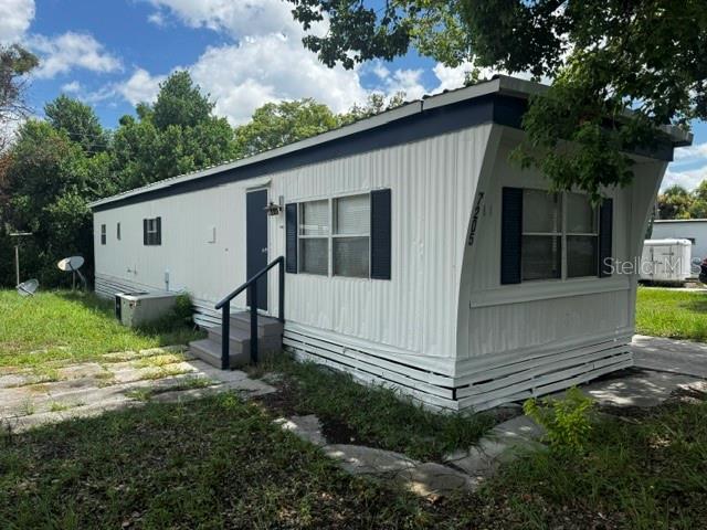A white mobile home with dark shutters sits on a grassy lot under a blue sky — 7205 COMMONS BOULEVARD, PORT RICHEY, FL
