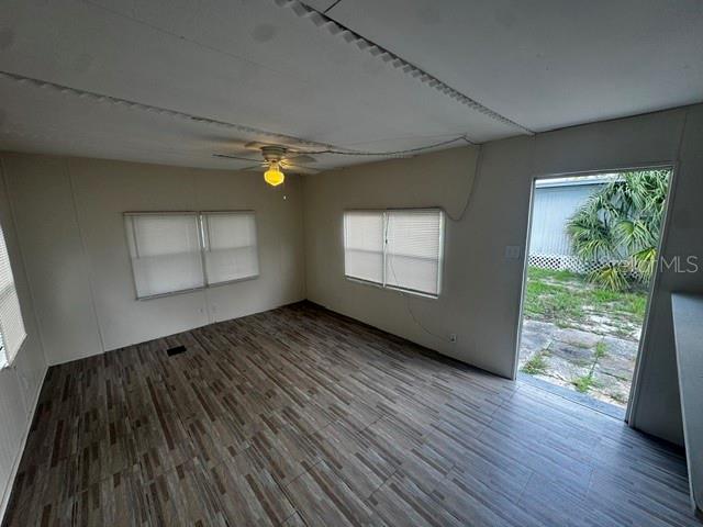 An empty room features wood-look tile flooring, a ceiling fan, and a door to outside — 7205 COMMONS BOULEVARD, PORT RICHEY, FL