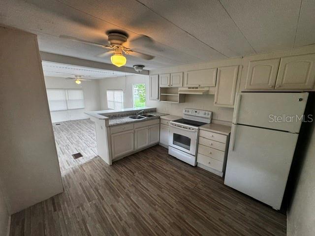 A kitchen with white cabinets, a white refrigerator, and a stove overlooks a living area — 7205 COMMONS BOULEVARD, PORT RICHEY, FL