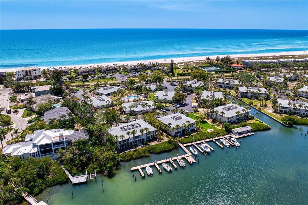 Two blue Adirondack chairs sit on a concrete patio overlooking a canal with boat docks — 6700 GULF OF MEXICO DRIVE UNIT 118, LONGBOAT KEY, FL