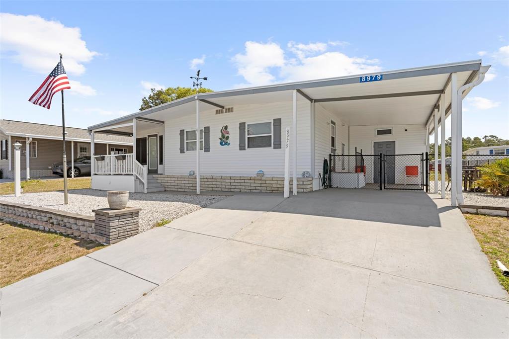 A white single-story manufactured home features a concrete driveway, a carport, and an American flag — 8979 HIGHPOINT BOULEVARD, BROOKSVILLE, FL