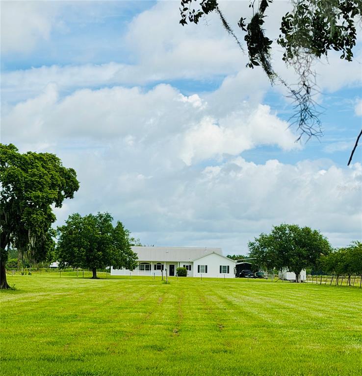 A white single-story house sits in the middle of a large, grassy field — 9120 COUNTY ROAD 304, BUNNELL, FL