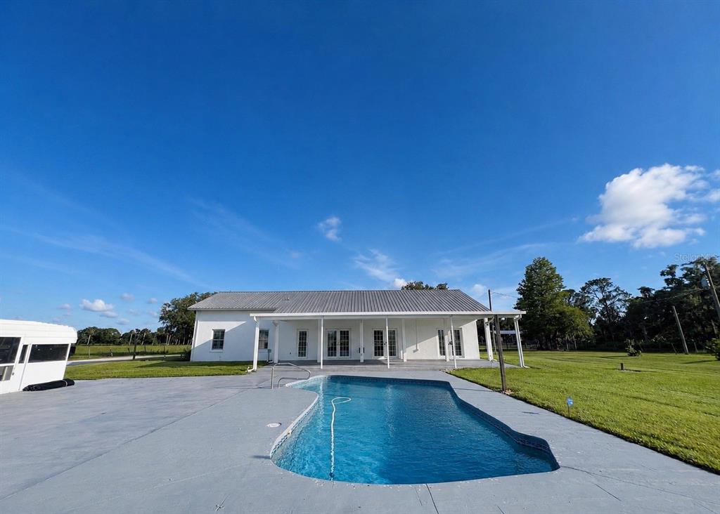 A white house with a metal roof sits behind a swimming pool on a lawn — 9120 COUNTY ROAD 304, BUNNELL, FL