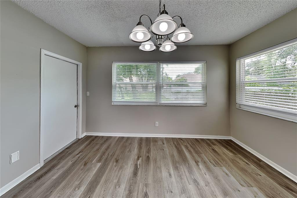 An empty dining room features wood-look flooring, a central chandelier, and two windows with blinds — 1404 FERNWOOD PLACE, SEFFNER, FL