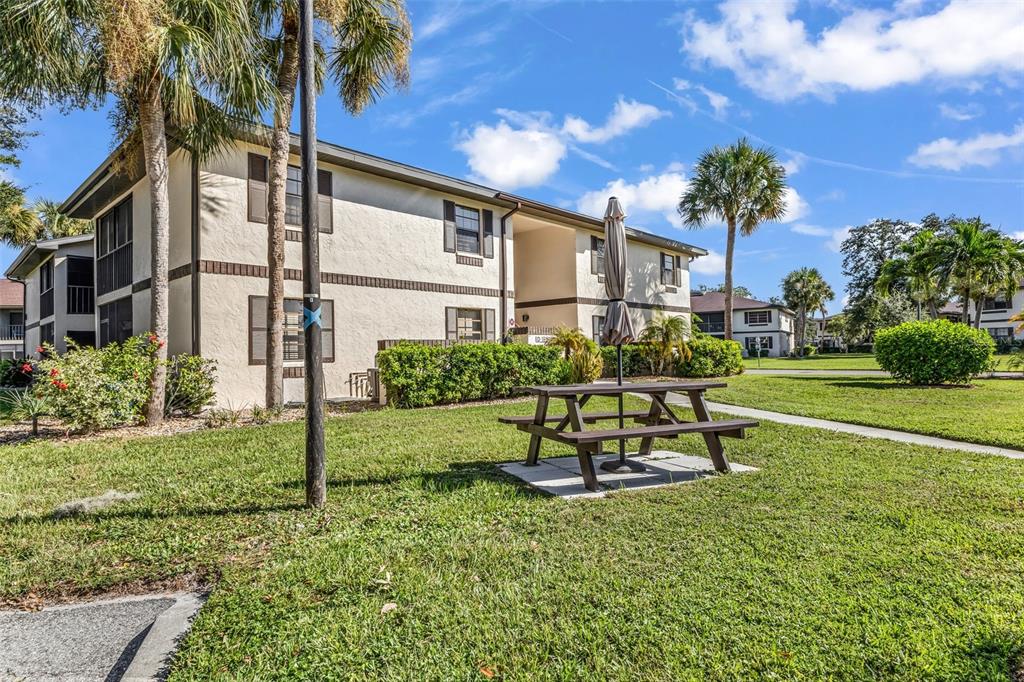 A two-story apartment building with a picnic table on a grassy lawn in the foreground — 19505 QUESADA AVENUE UNIT D202, PORT CHARLOTTE, FL