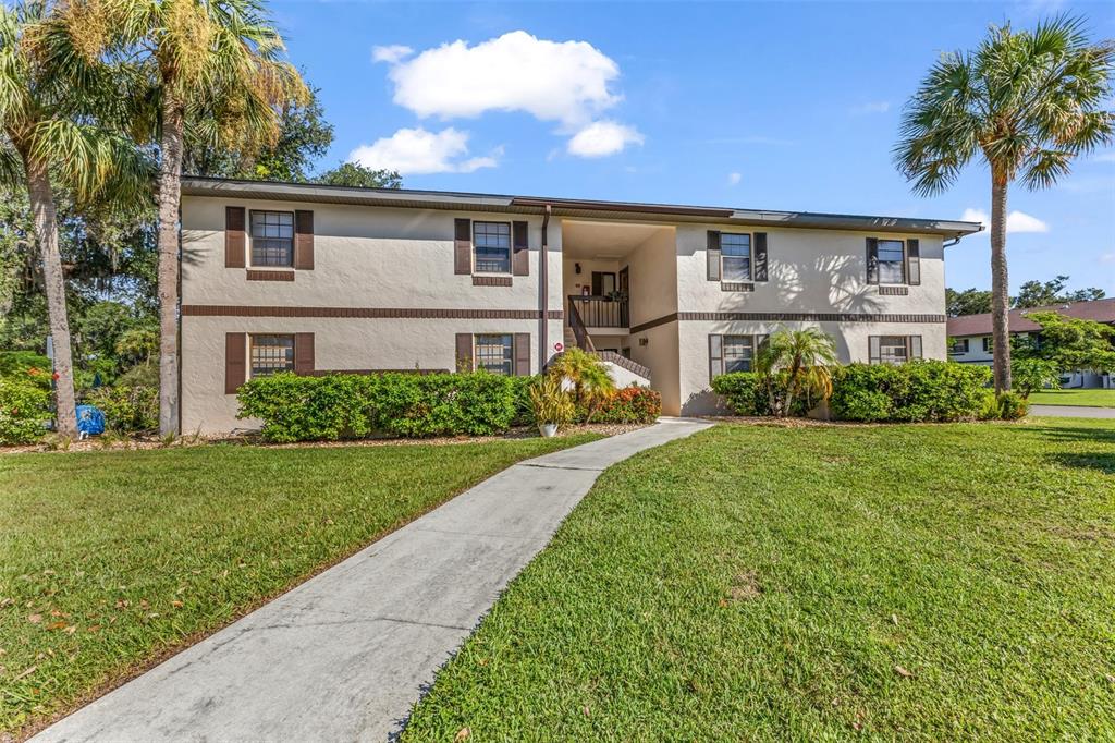 A two-story apartment building with a central walkway and palm trees on a sunny day — 19505 QUESADA AVENUE UNIT D202, PORT CHARLOTTE, FL