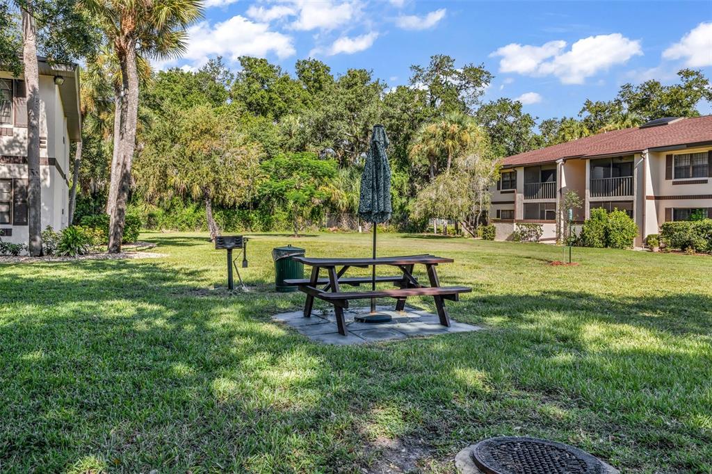 A picnic table with an umbrella and a charcoal grill sit on a grassy lawn — 19505 QUESADA AVENUE UNIT D202, PORT CHARLOTTE, FL