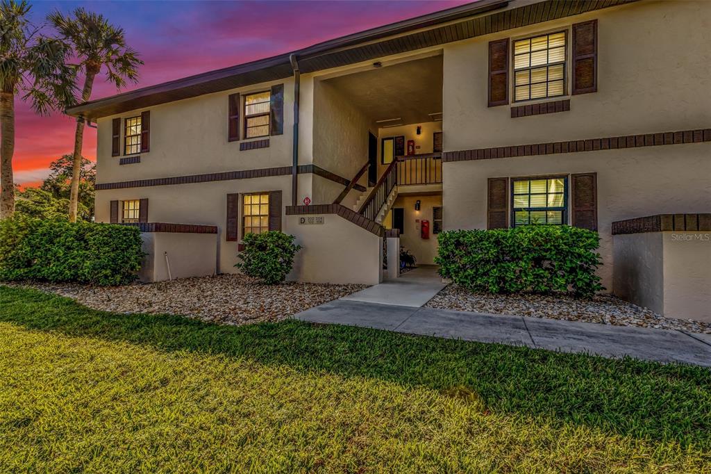A two-story apartment building exterior features tan stucco walls, brown shutters, and a central staircase — 19505 QUESADA AVENUE UNIT D202, PORT CHARLOTTE, FL