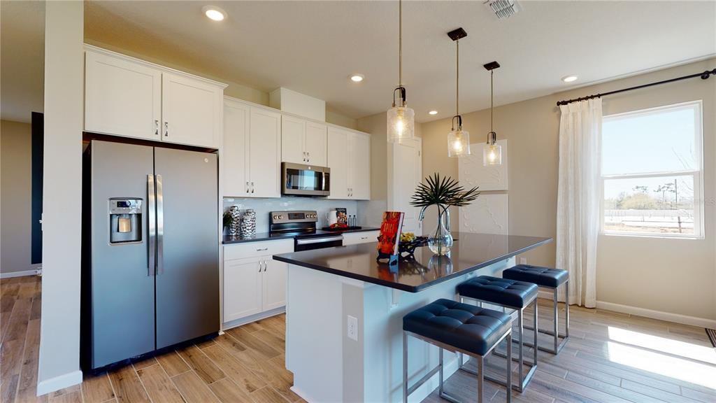 A modern kitchen features white cabinetry, stainless steel appliances, a dark island, and bar stools — 5311 SPRING MAIDEN CIRCLE, APOLLO BEACH, FL