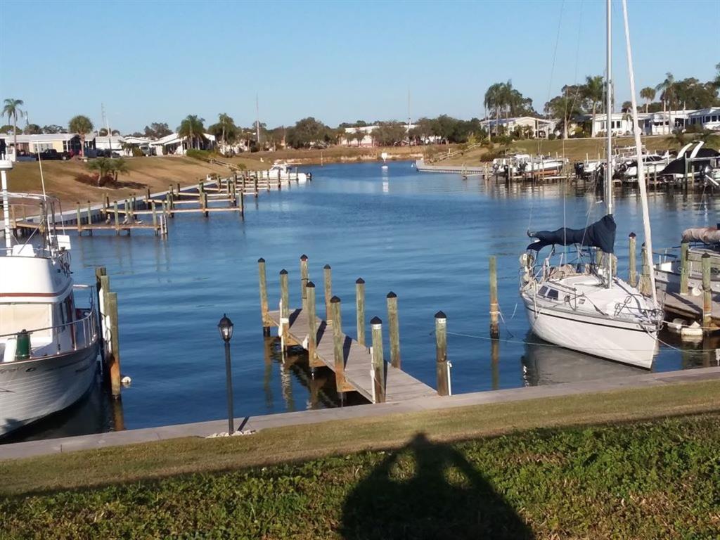 A canal view featuring a wooden dock, several moored boats, and a grassy shoreline — 811 BOGIE, VENICE, FL