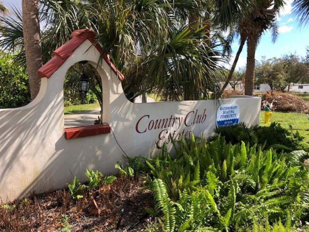A stucco entrance sign for Country Club Estates features a decorative archway and lush landscaping — 811 BOGIE, VENICE, FL