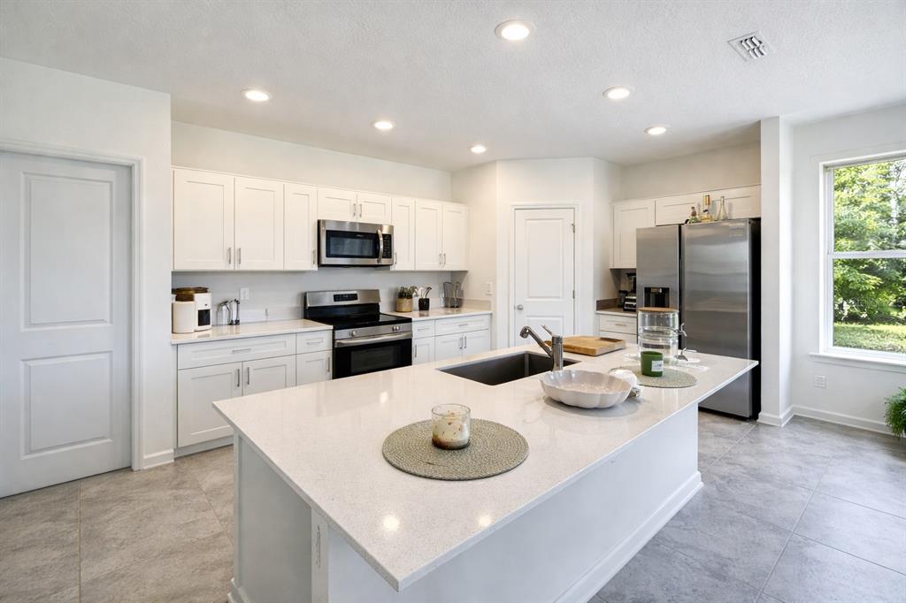 A modern kitchen features white cabinets, stainless steel appliances, a large island, and tile flooring — 1824 FOREMAN RD, EAGLE LAKE, FL