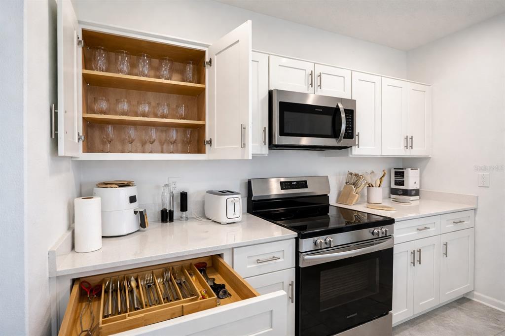 A kitchen features white cabinets, stainless steel appliances, quartz countertops, and an open utensil drawer — 1824 FOREMAN RD, EAGLE LAKE, FL