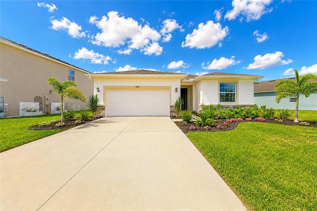 A single-story house with a white garage, light-colored stucco exterior, and a concrete driveway — 12432 DORA TRAIL, PARRISH, FL