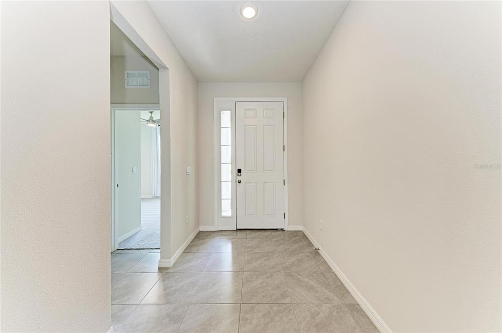 A bright entryway features light-colored tile flooring, beige walls, and a white front door — 12432 DORA TRAIL, PARRISH, FL