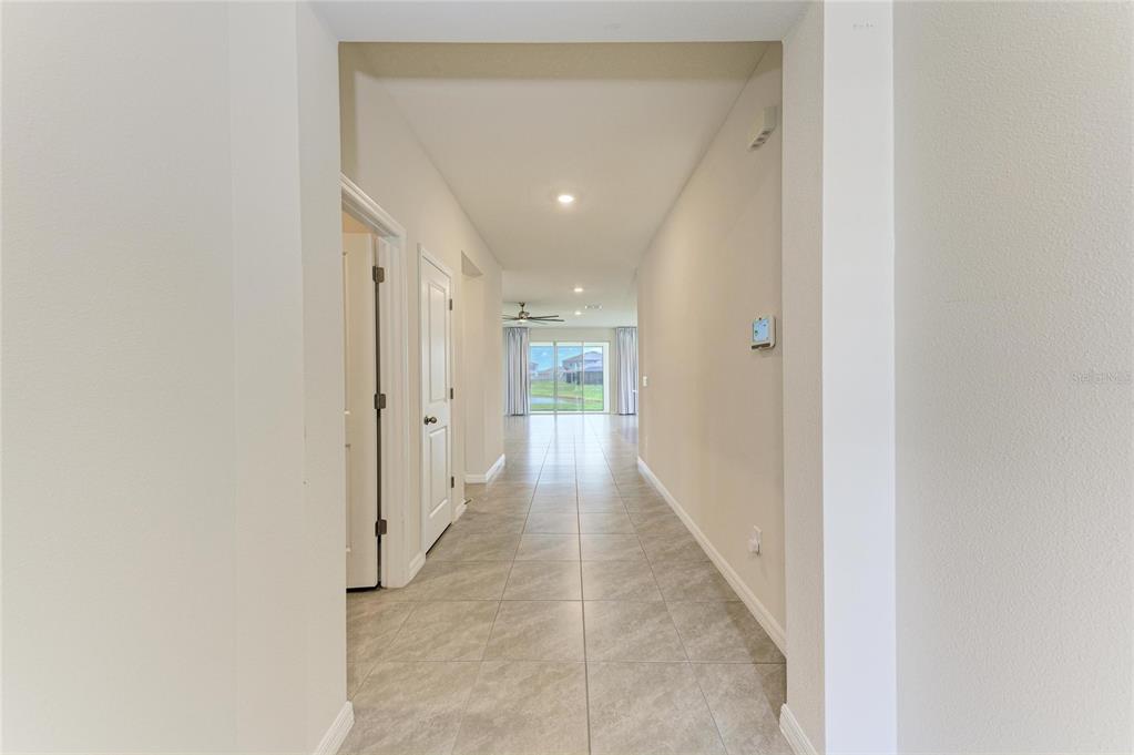 A tiled hallway leads to a living area with sliding glass doors overlooking a pond — 12432 DORA TRAIL, PARRISH, FL