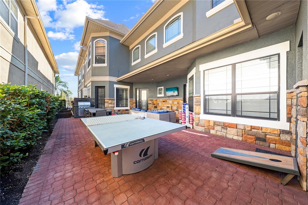 A patio features a ping pong table, cornhole board, outdoor furniture, and stone wall accents — 785 GOLDEN BEAR DRIVE, REUNION, FL